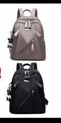 Two backpacks shown on a plain white background: one taupe-gray and one black, each with top handles, front zip compartments, side pockets, and hanging keychains.